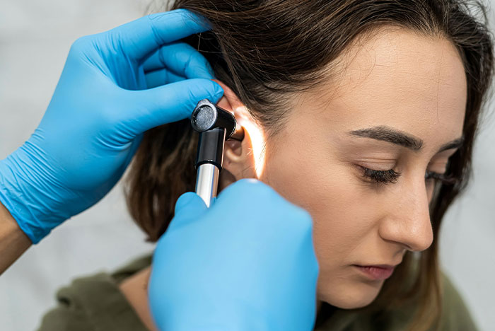 A woman receiving an ear examination from a medical professional wearing blue gloves, focusing on potential concussion symptoms.