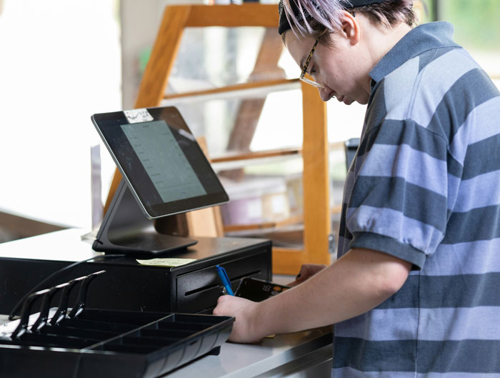 Person at a cash register writing a note, representing reasons for being fired in a work setting.