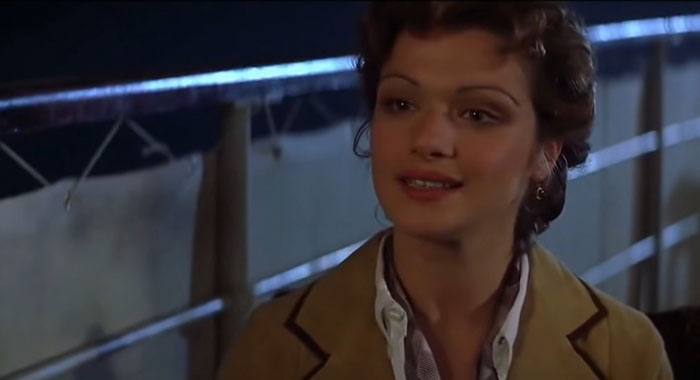 A strong female protagonist smiling warmly, wearing a brown coat on a ship deck at night.