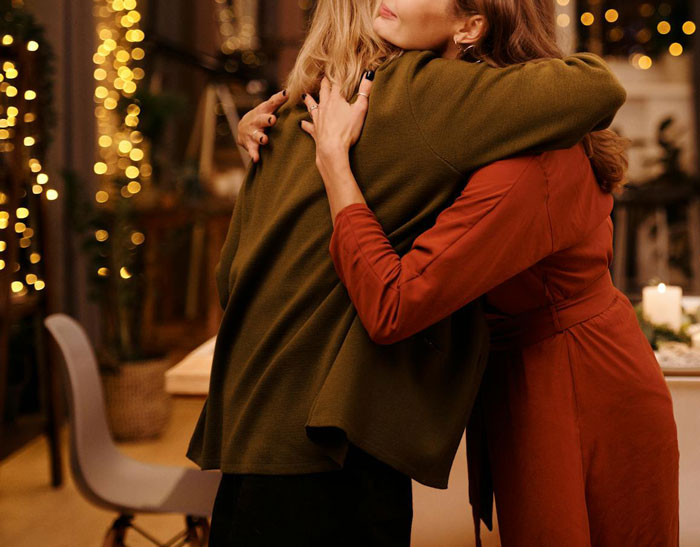 Two women hugging warmly in a festive, softly lit room, evoking themes of family and forgiveness during Thanksgiving.