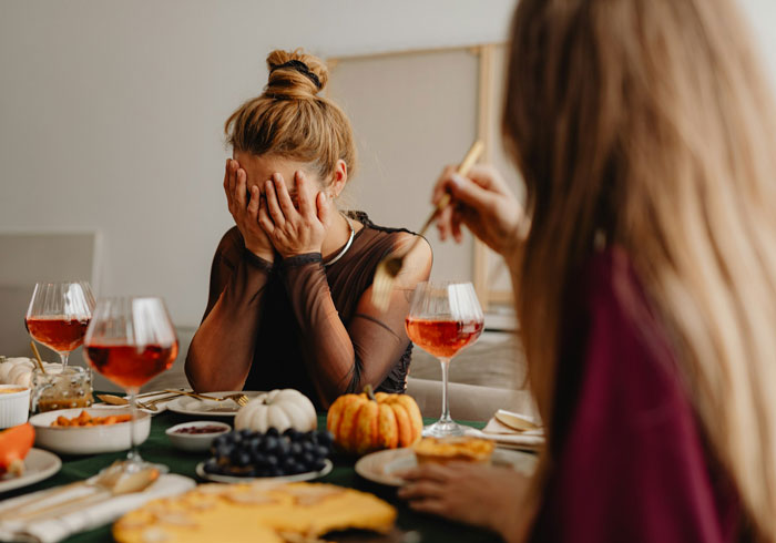 Woman upset at Thanksgiving dinner table with food and wine, highlighting family tension and emotional distress.