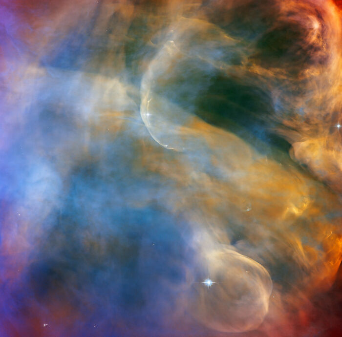 Colorful nebula with swirling clouds of gas and dust in space, featuring vibrant blues, oranges, and greens.