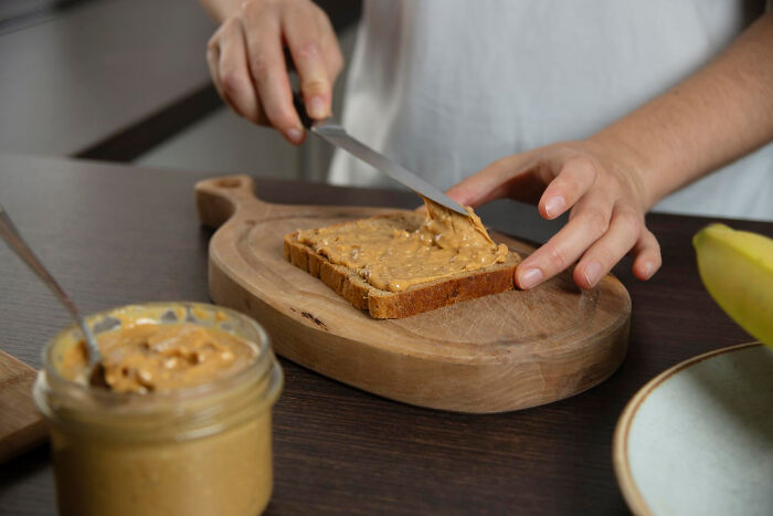 Person spreading peanut butter on toast, illustrating partner's weird habit in kitchen setting.