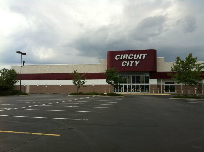 Empty parking lot in front of a closed Circuit City store under a cloudy sky.