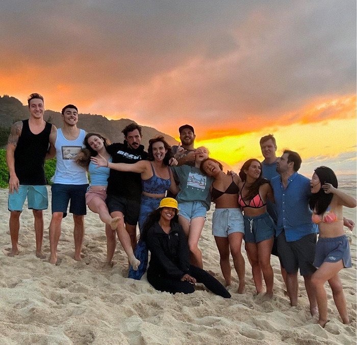 Luigi Mangione with friends on a sandy beach at sunset, embracing and smiling.