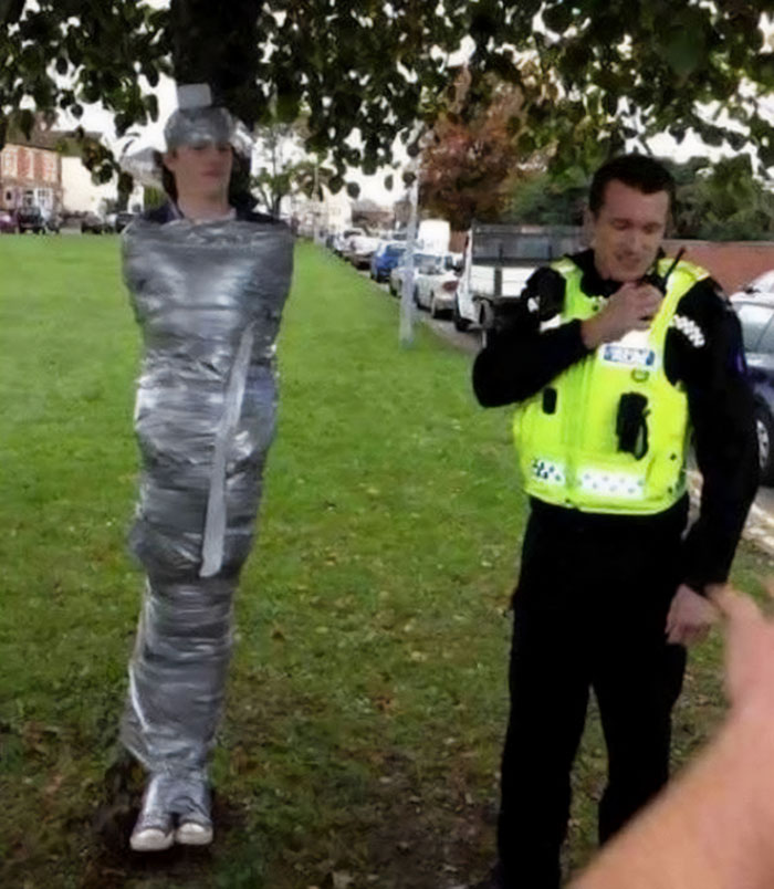 A person wrapped in duct tape to a tree while a police officer stands nearby, exemplifying cursed images.