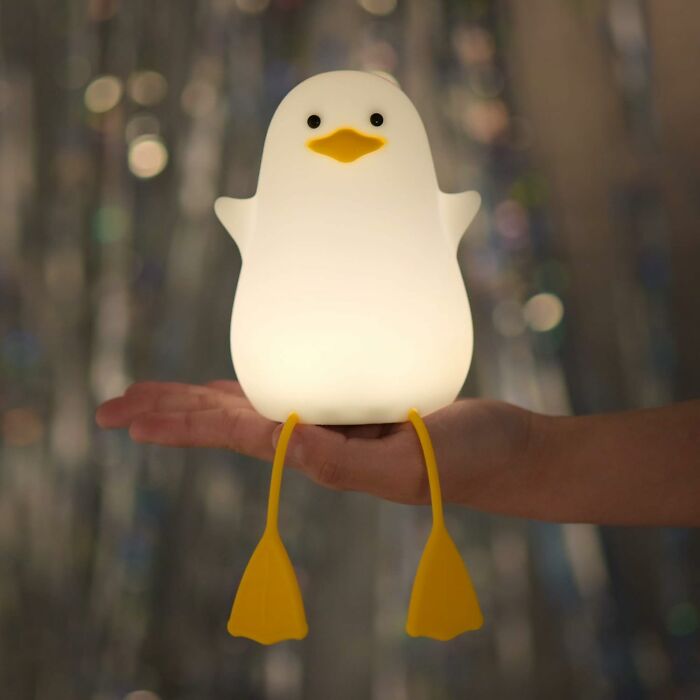 Cute glowing penguin lamp with yellow feet held in a person's hand.