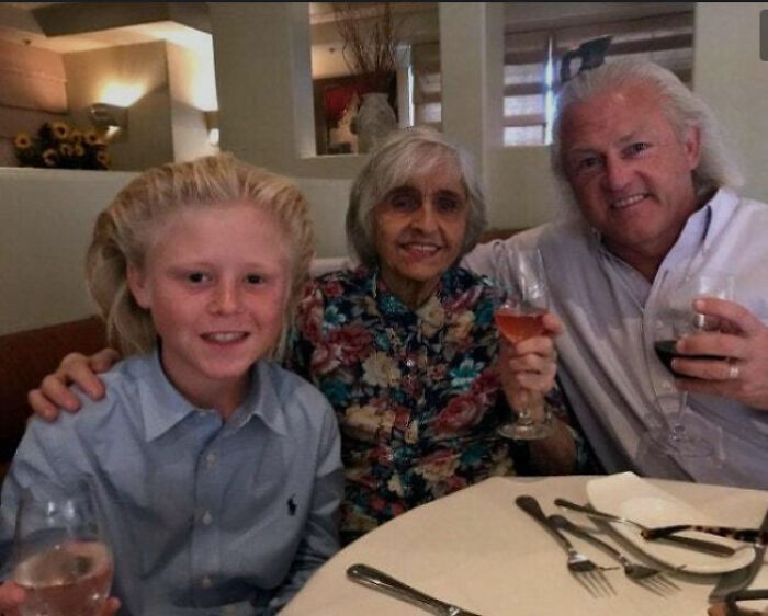 Family with unique hairstyles smiling and holding wine glasses at a restaurant.