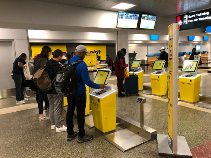 People using self-service kiosks at an airport, illustrating deceptive marketing techniques in consumer experiences.