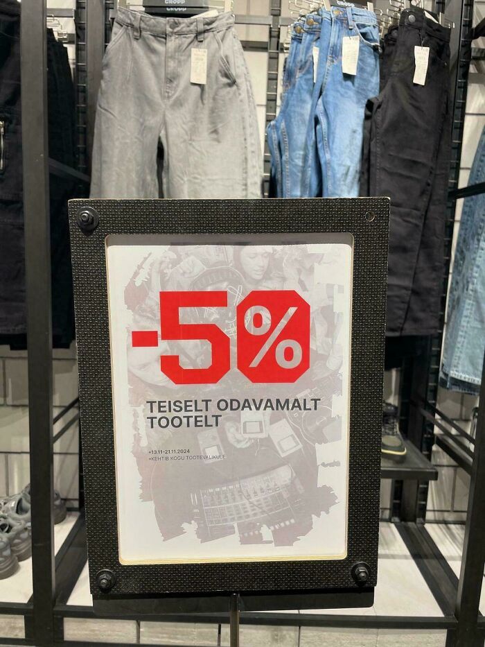 Sign with a deceptive marketing technique offering a 5% discount, displayed in front of hanging jeans in a store.