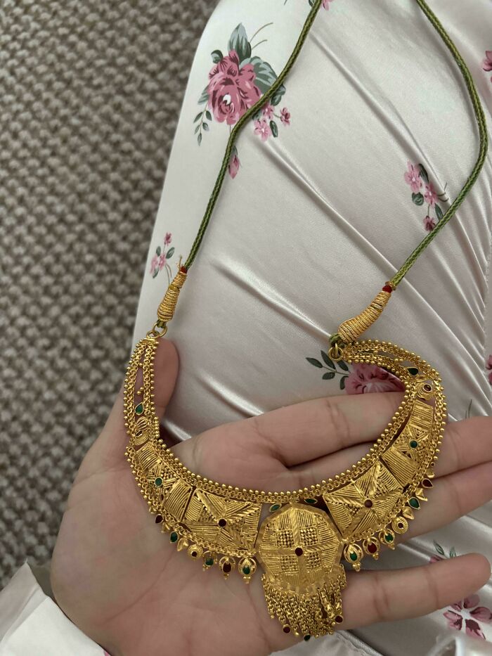 A hand holding a gold necklace with intricate designs, showcasing a unique inheritance piece.