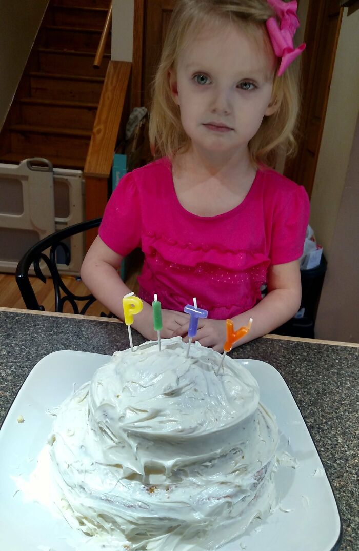 Little girl in pink shirt, standing by a cake with funny candles, embodying hilarious in-laws humor.