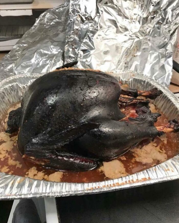 Burnt turkey in a foil roasting pan, showcasing a common hilarious in-laws cooking mishap.