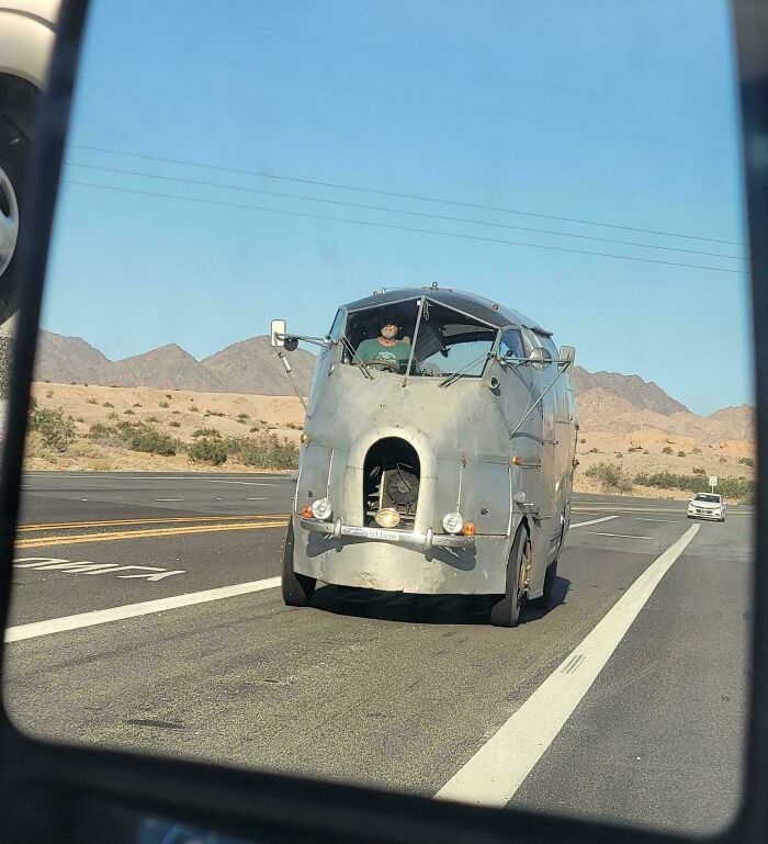 Unusual vehicle on the road, resembling a futuristic design, driving on a clear day.