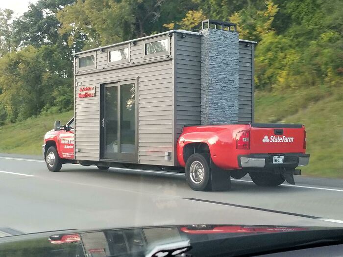 Truck carrying a small house with chimney on road, showcasing interesting things while driving.