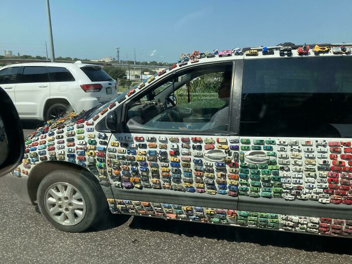 Van covered with toy cars driving on the road, showcasing interesting things on the road.