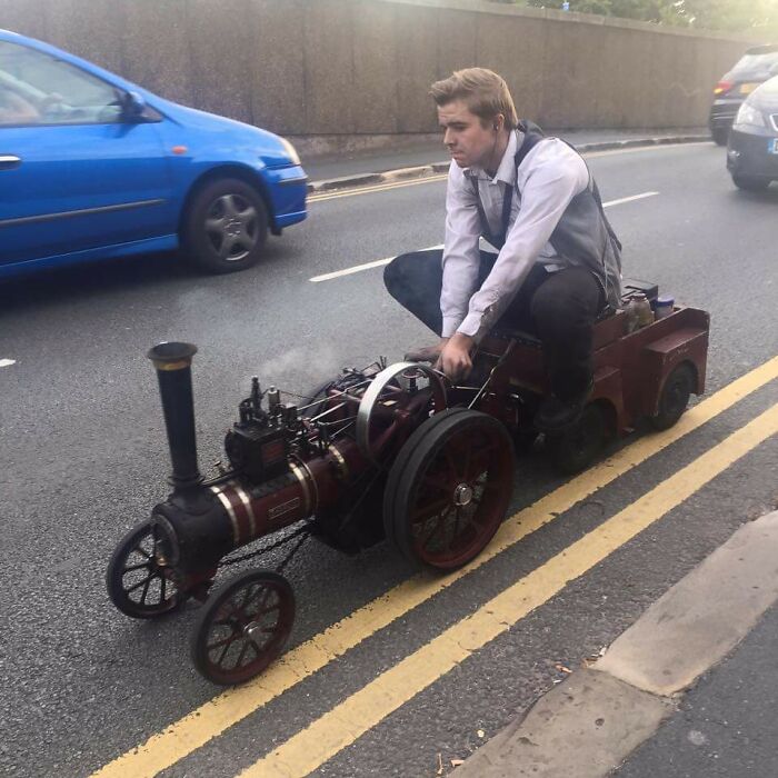 Man rides tiny steam-powered vehicle on road, showcasing interesting things.