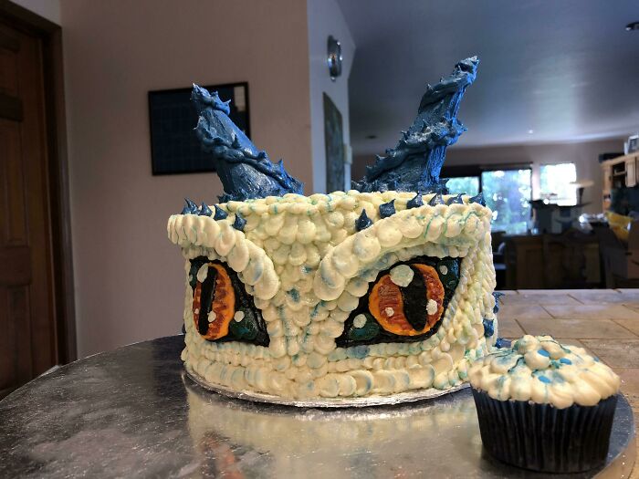 Dragon-themed cake with detailed icing eyes and scales, accompanied by a matching cupcake. Foodies will love the design.