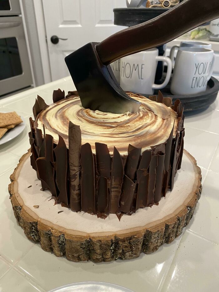 A cake decorated with chocolate shards, designed to look like a chopped log, featuring an edible axe for foodies to love.