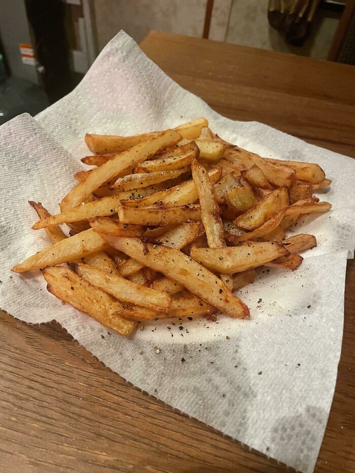 Golden crispy French fries seasoned with black pepper on a paper towel, perfect for foodies who love beautiful food.