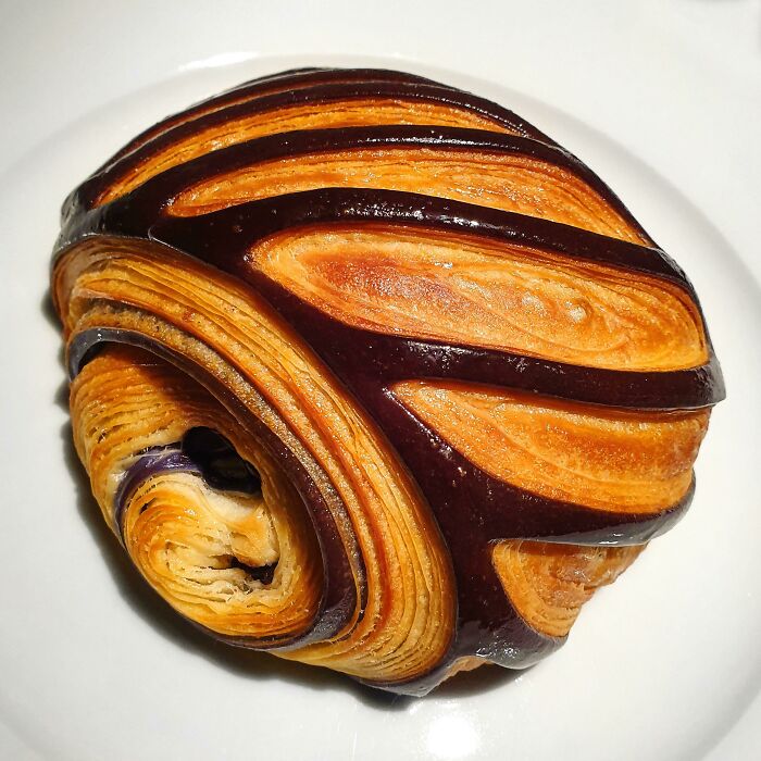 Beautiful food pic of a golden, flaky pastry with dark chocolate stripes on a white plate.