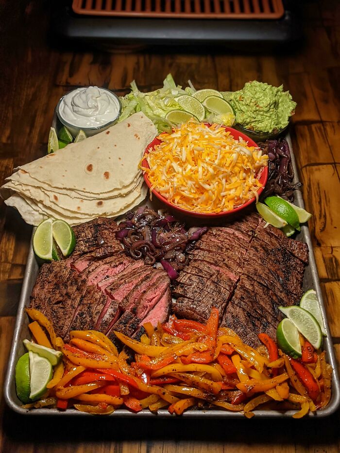 Delicious grilled steak fajitas with tortillas, cheese, peppers, and lime on a tray, perfect for foodies to love.