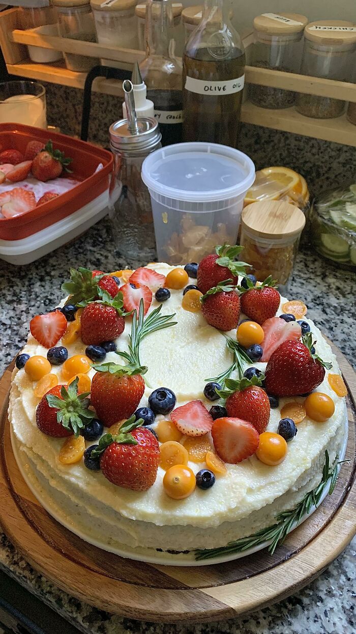 Beautiful cake adorned with strawberries, blueberries, and rosemary, perfect for foodies to love.