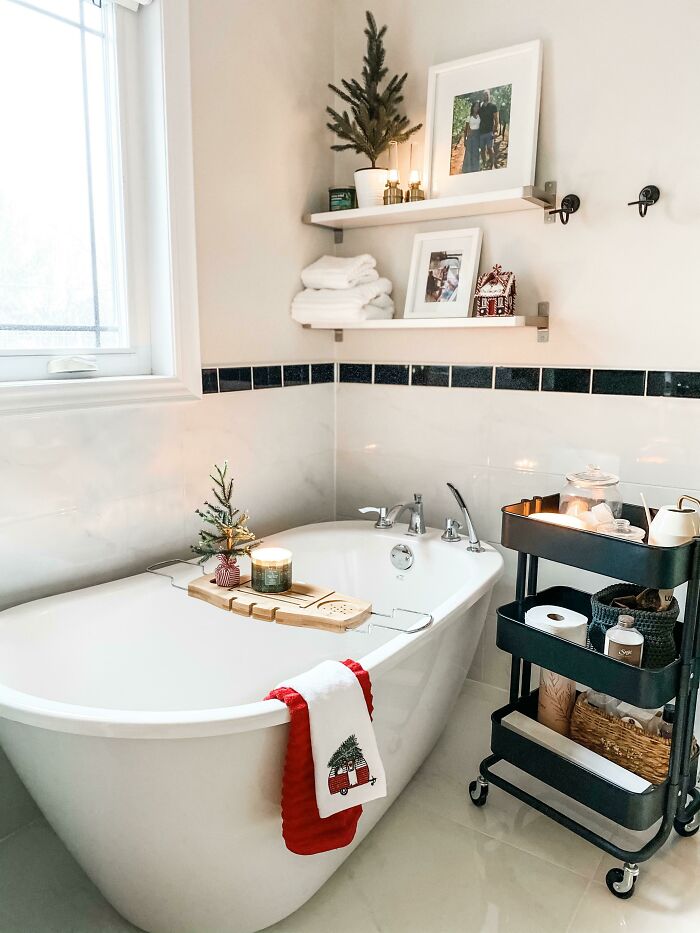 Christmas-decorating-ideas in a bathroom with a festive towel, mini tree, and candles on a tub tray for cozy ambiance.