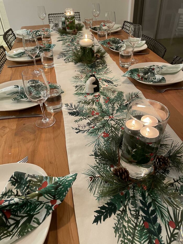 Christmas decorating ideas with a festive table setting, featuring candles, pine branches, and holly-themed napkins.