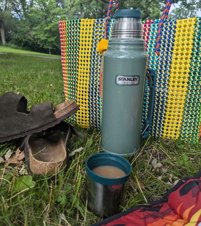 Vintage thermos inheritance on grass with colorful woven bag and sandals.