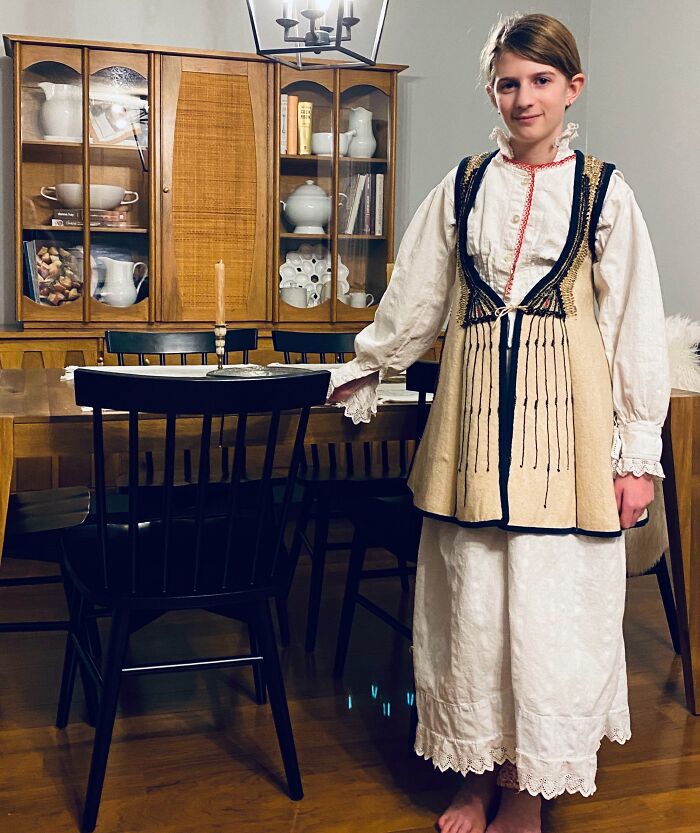 Person wearing traditional attire inherited from family, standing in a dining room with wooden furniture in the background.