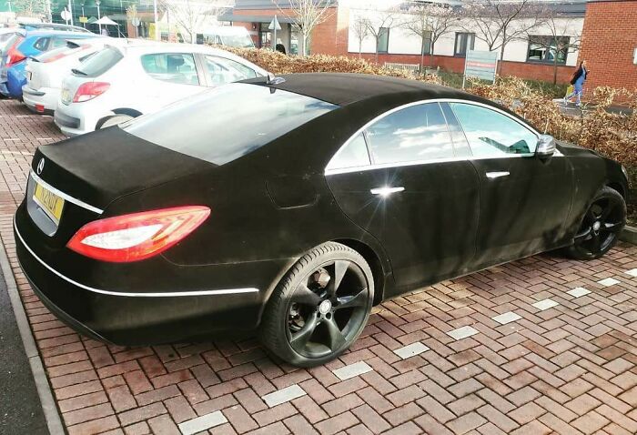 Matte black car with mismatched rims parked awkwardly, an example of car-fails.