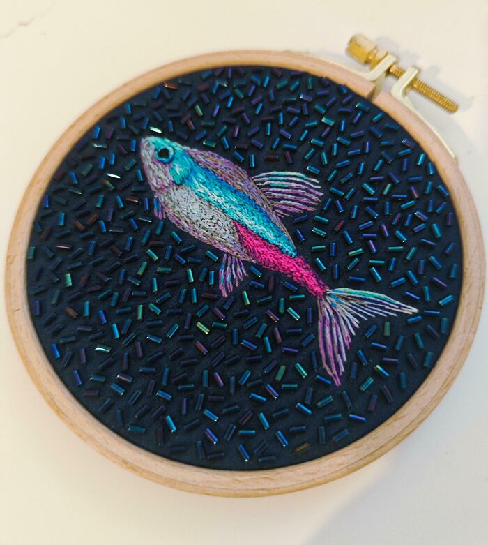 Creative embroidery of a colorful fish on dark fabric in a wooden hoop.