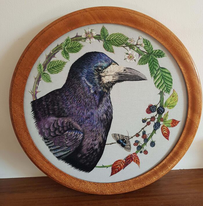 Creative embroidery of a detailed raven surrounded by colorful leaves, mounted in a wooden frame.