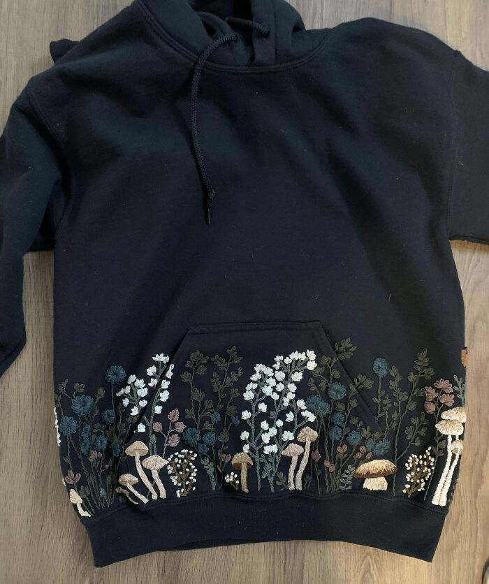 Black hoodie with creative embroidery of mushrooms and flowers on the front pocket.