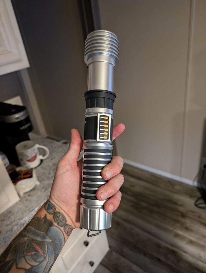 Tattooed hand holding a novelty lightsaber resembling a flashlight, capturing the essence of good fun with funny bosses.