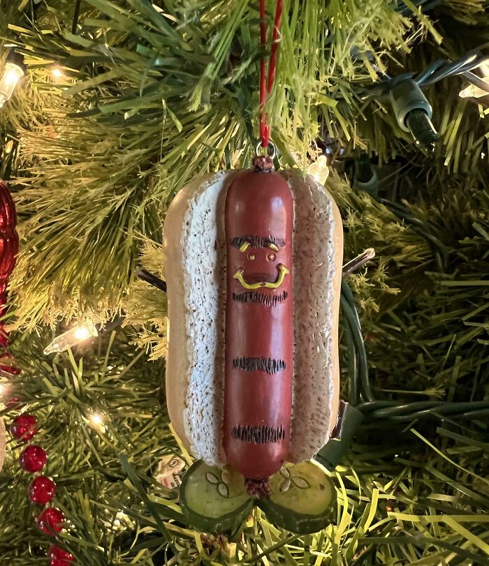 Funny hot dog ornament with a smiling face, hanging on a Christmas tree, representing good-funny-bosses humor.