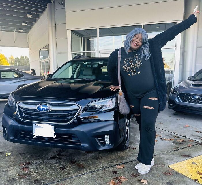 Person posing happily beside a black car, capturing a moment of joy.