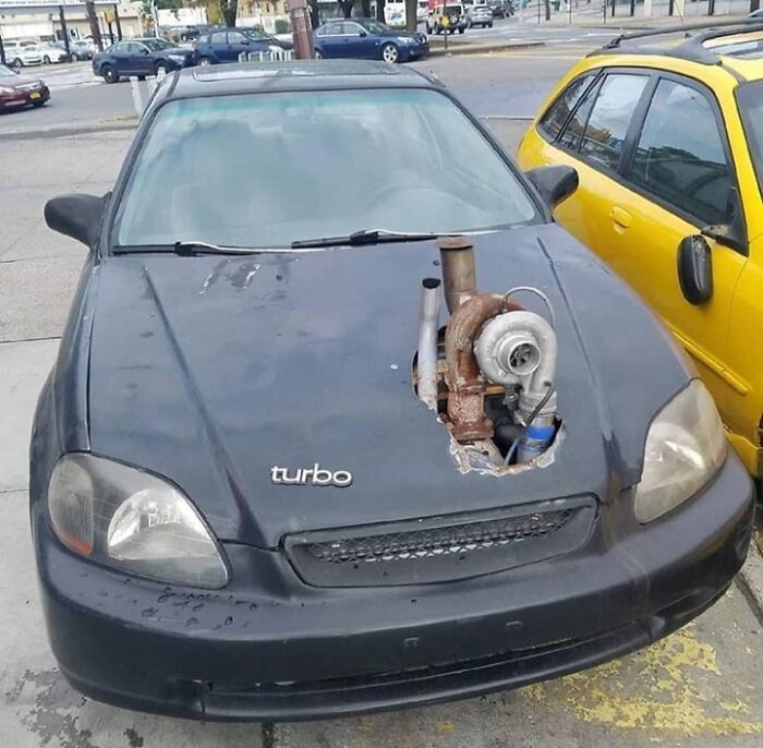 Car-fails showcase with exposed turbo on a black sedan, parked in a lot next to a yellow car.