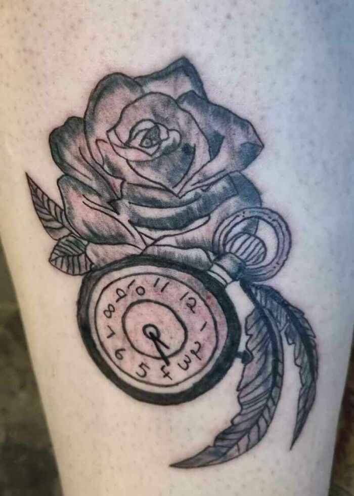 Tattoo fail of a distorted clock with a rose and feather design on skin.