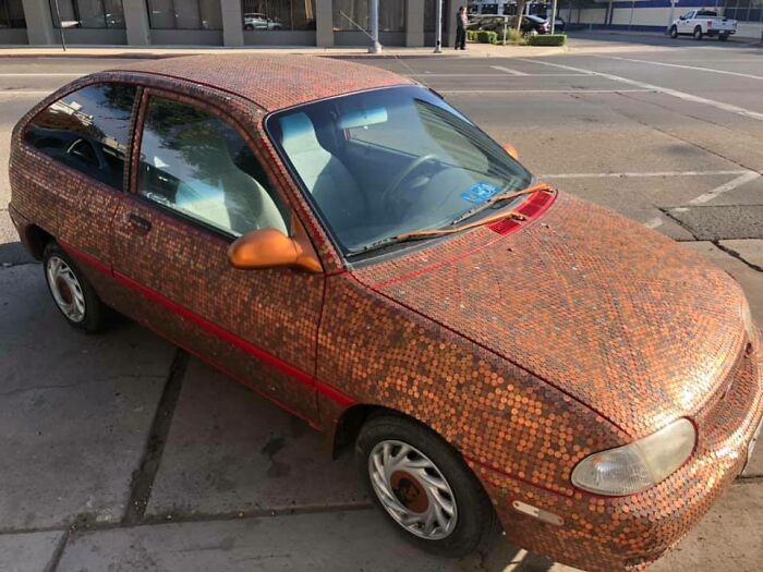 Car covered in pennies parked on a street, showcasing a unique car fail with creative but impractical decoration.