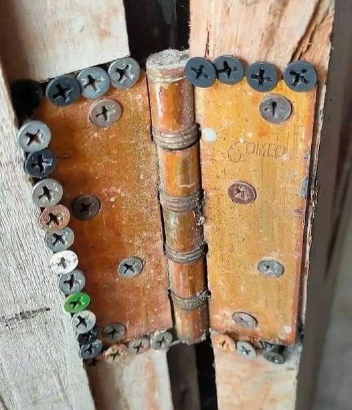 Hinges overloaded with mismatched screws in a wooden doorframe, showcasing cheap construction fails.