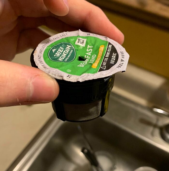 Hand holding a coffee pod with a hidden plastic mesh, illustrating deceptive marketing techniques in packaging.