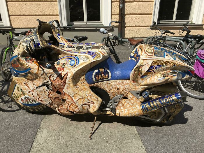 Artistic motorcycle with intricate designs parked on the street, capturing a unique car-fails theme.