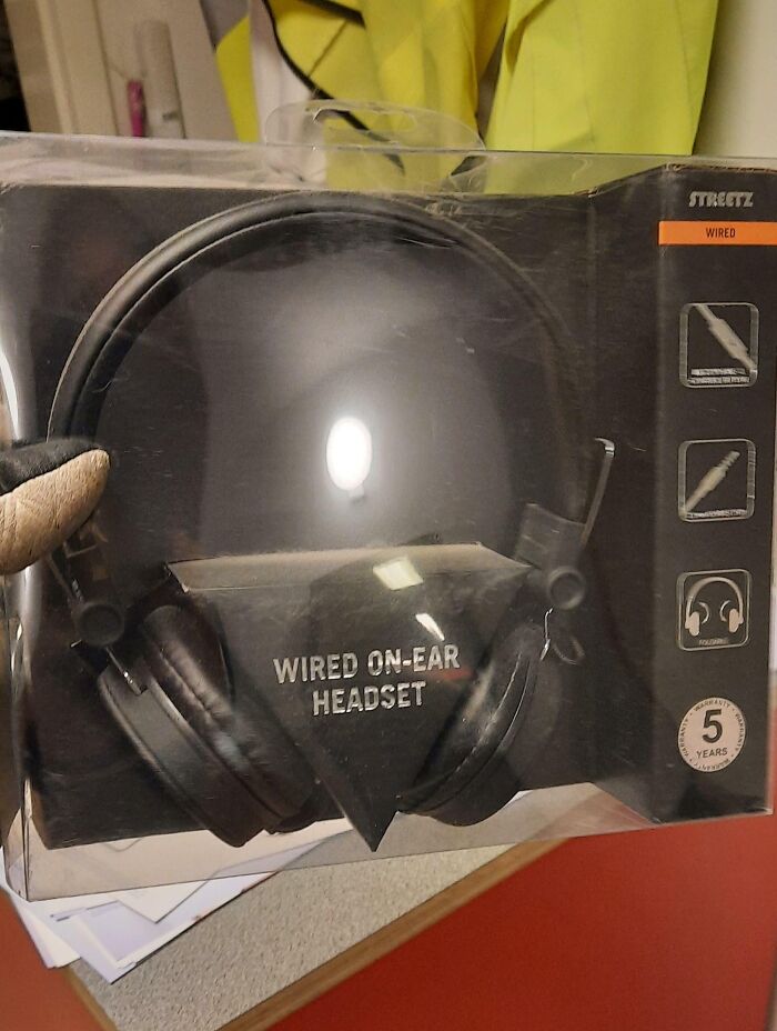 A wired on-ear headset in packaging, reflecting light, with a glove holding the box, related to Good-Funny-Bosses.