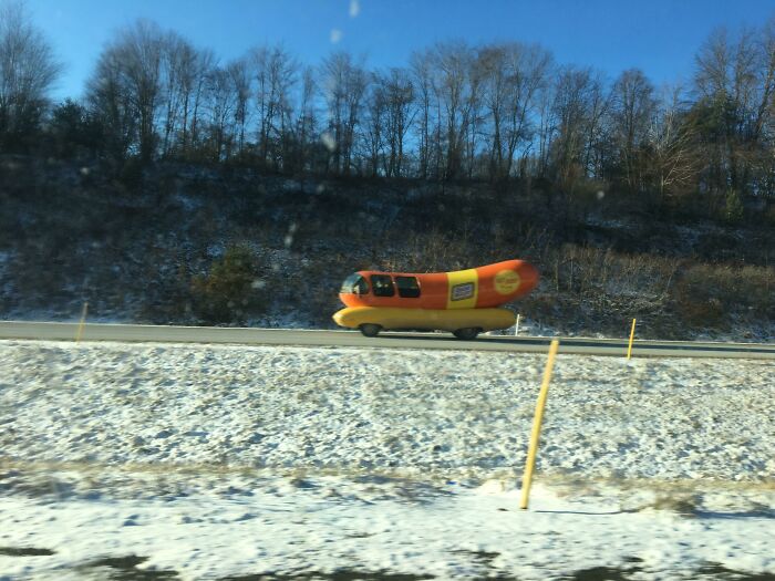 Hot dog-shaped vehicle driving on a snowy road, an interesting thing spotted on the road.