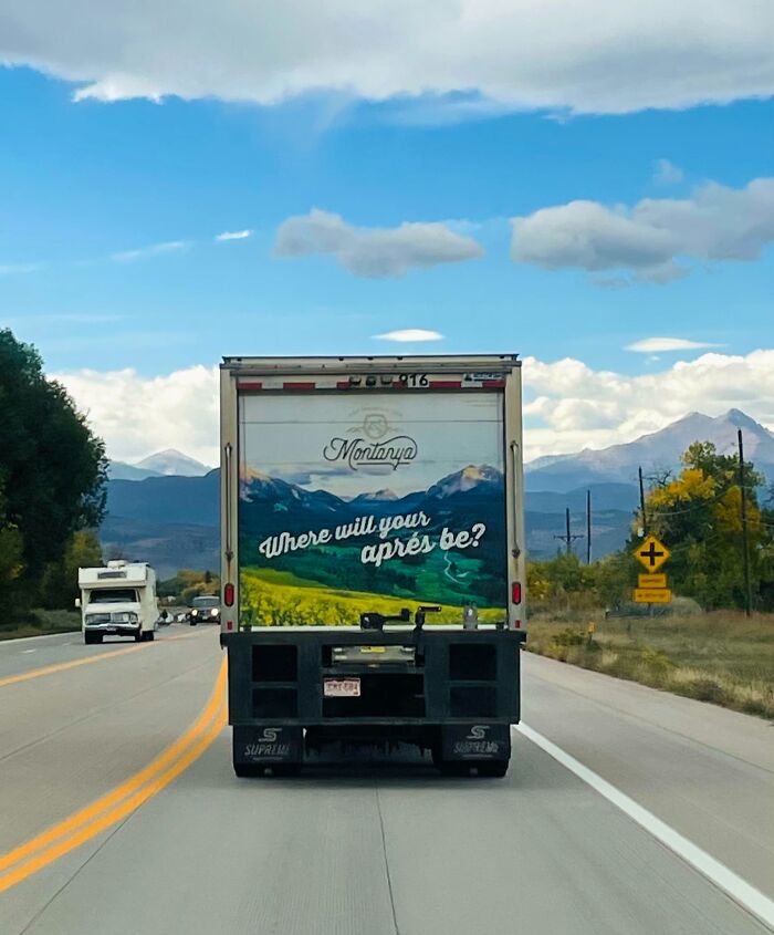 Truck with scenic mountain ad and text, "Where will your après be?" driving on a scenic road under blue sky.