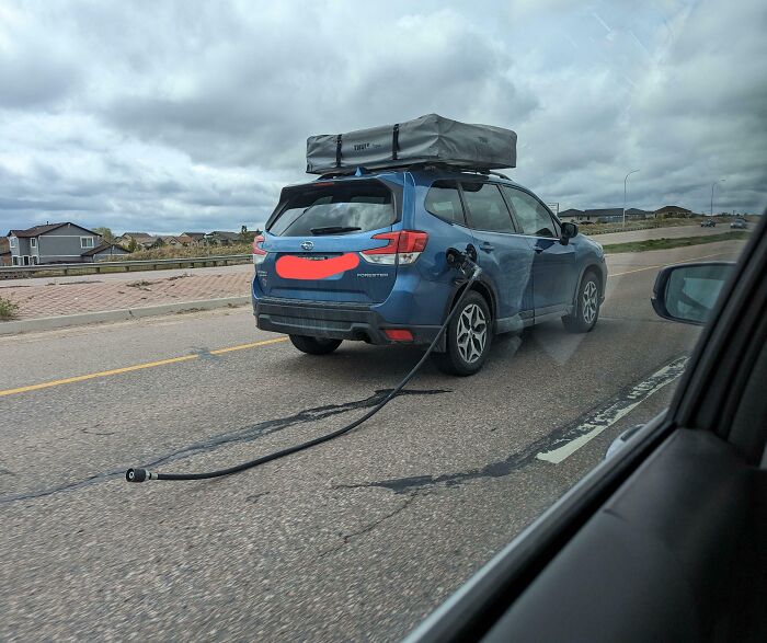 Blue SUV on the road with a gas hose attached, highlighting interesting travel mishaps.