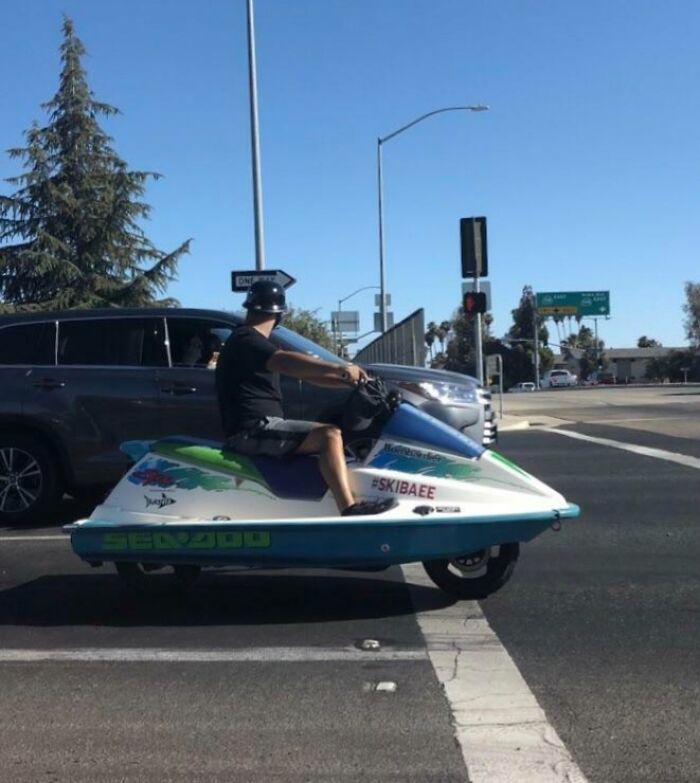 Man riding a modified jet ski on the road, an interesting thing spotted at an intersection under a clear blue sky.