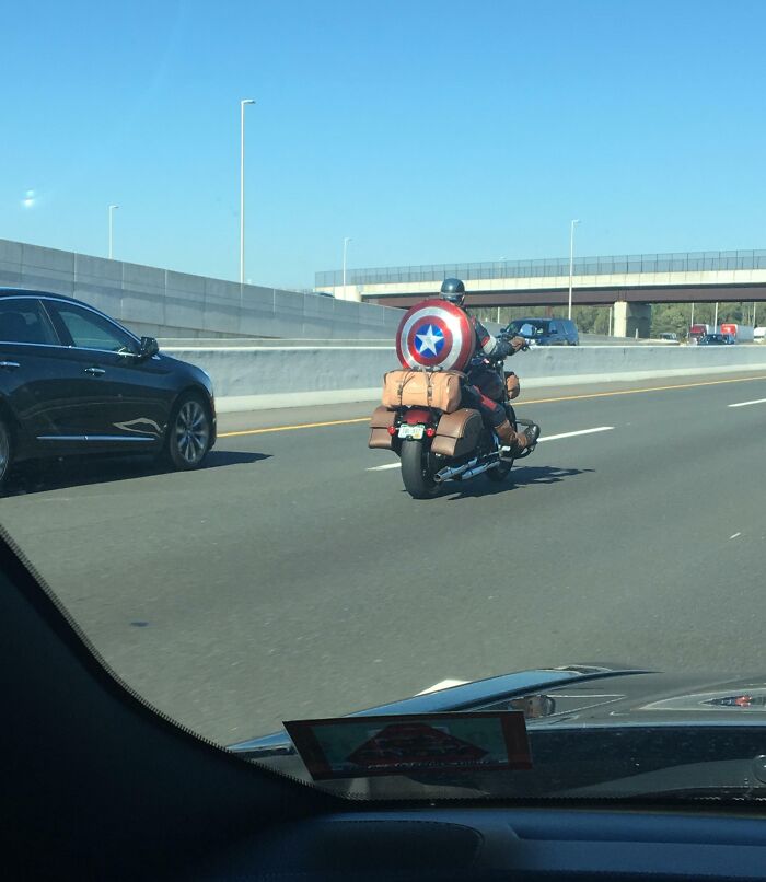 Motorcyclist on highway with Captain America shield; an intriguing sight on the road.